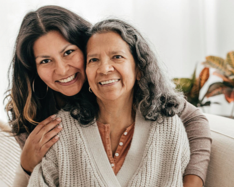 Foto de uma mãe idosa e filha adulta a sorrir para a câmara